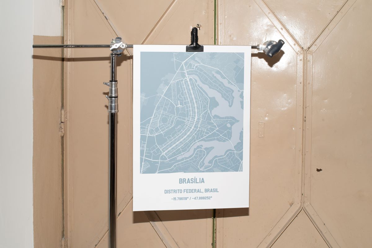 Poster de mapa personalizado digital de Brasília na cor azul, preso por uma pinça preta em um suporte de estúdio fotográfico profissional.