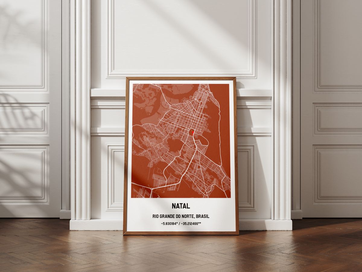 Quadro com moldura de madeira clássica mostrando o mapa personalizado da cidade de Natal na cor terracota, apoiado no piso de taco em frente a uma parede branca com boiserie.