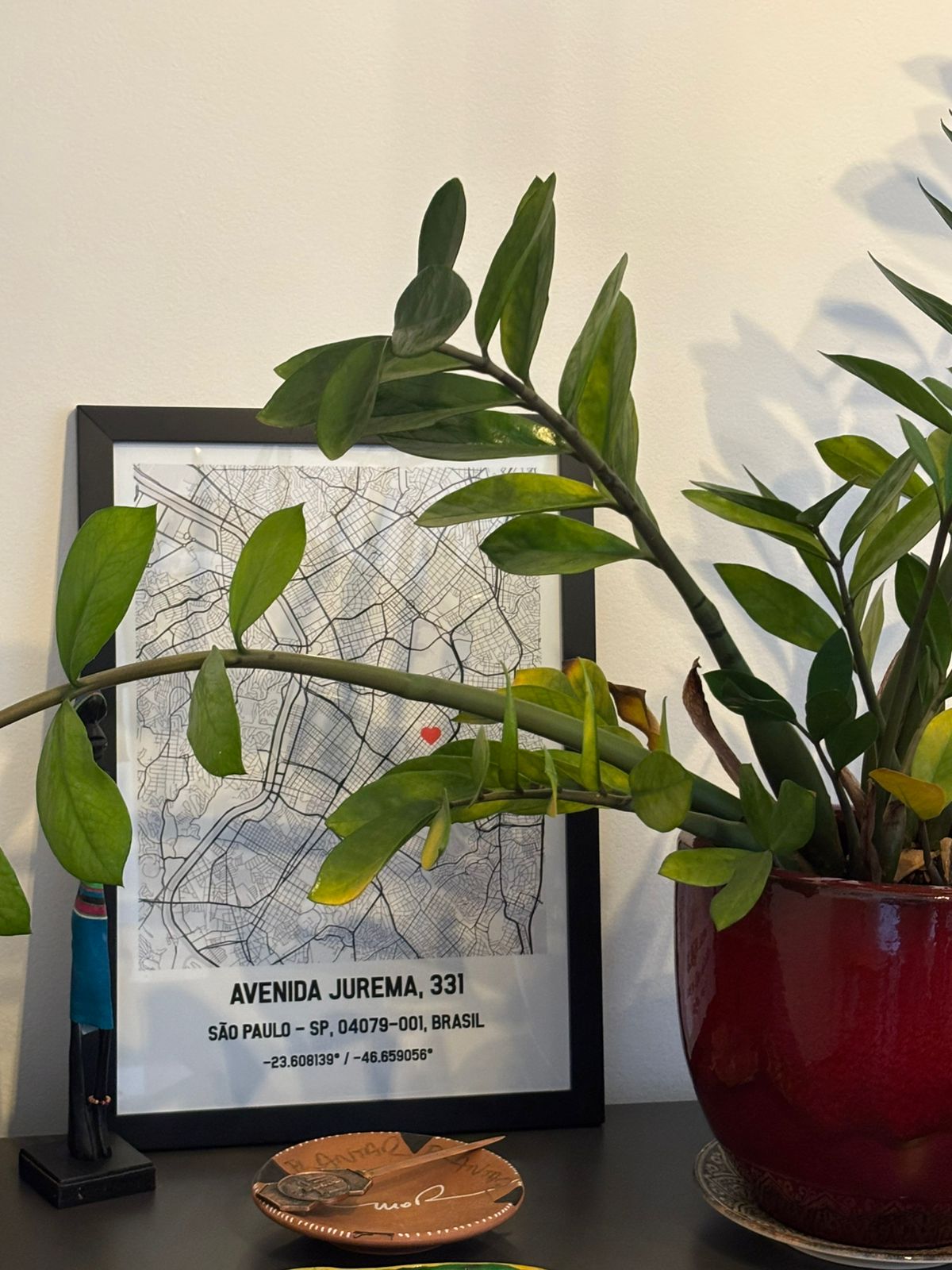 Quadro com moldura preta de mapa personalizado de São Paulo enviado por cliente, posicionado na decoração de uma casa ao lado de um vaso de planta verde.