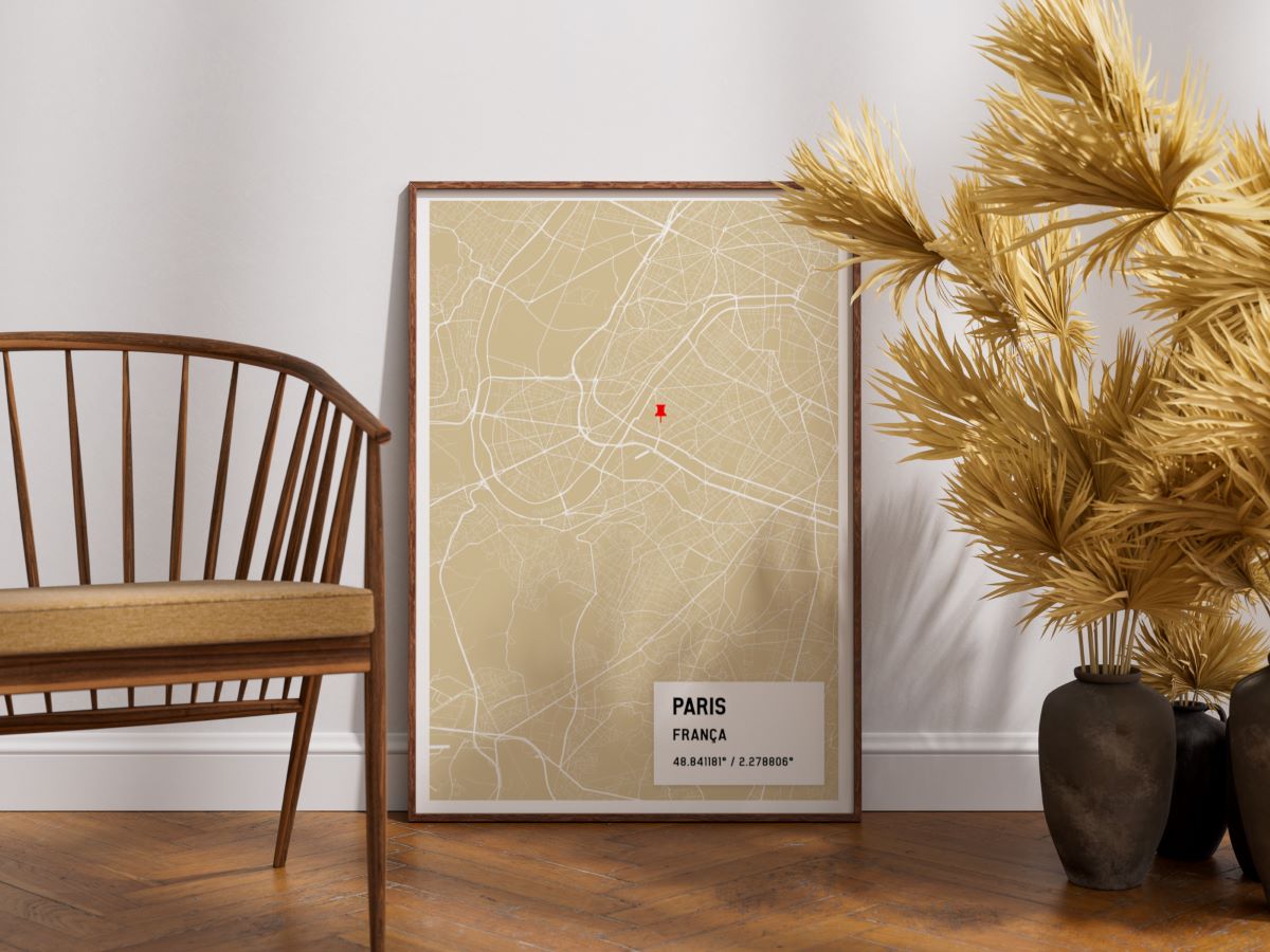 Quadro decorativo com moldura de madeira e mapa personalizado de Paris na cor mostarda, apoiado no chão de madeira ao lado de uma cadeira de design e vasos com plantas secas.